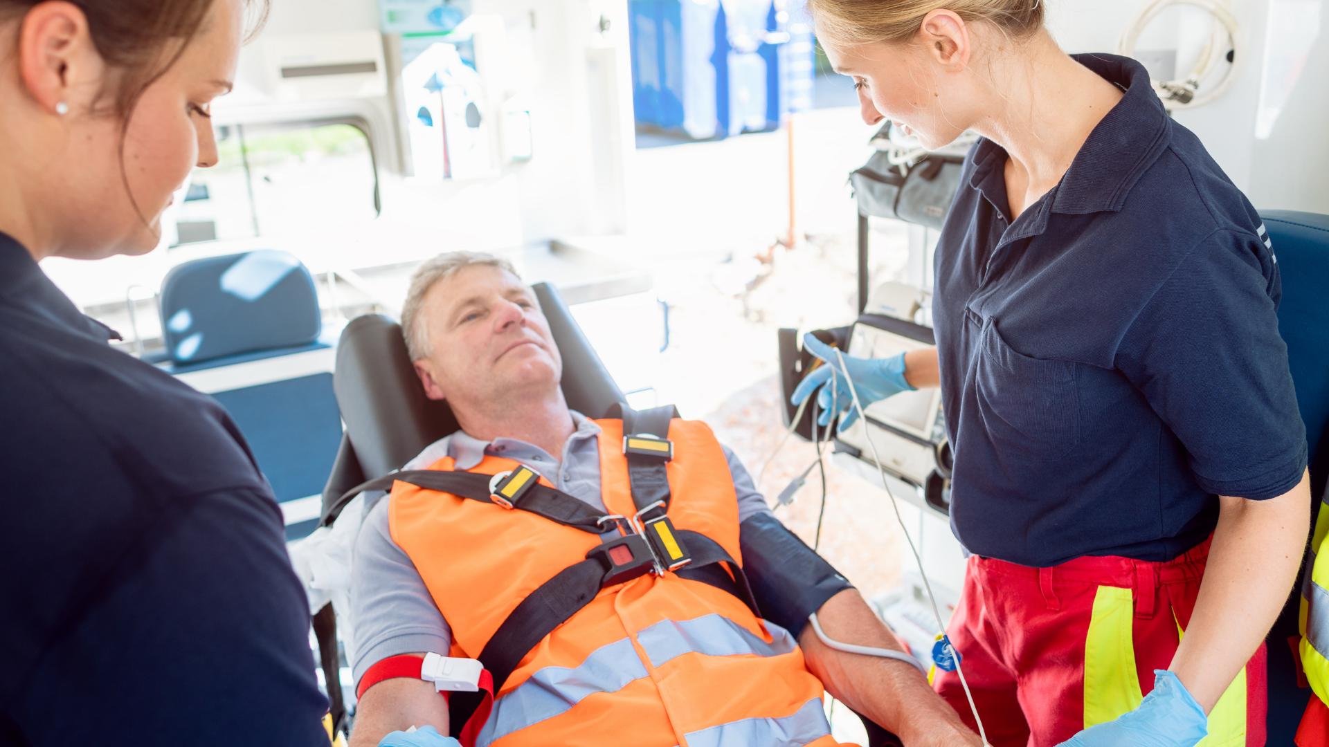 Emergency medical personnel attending to an older male patient on a stretcher inside an ambulance.